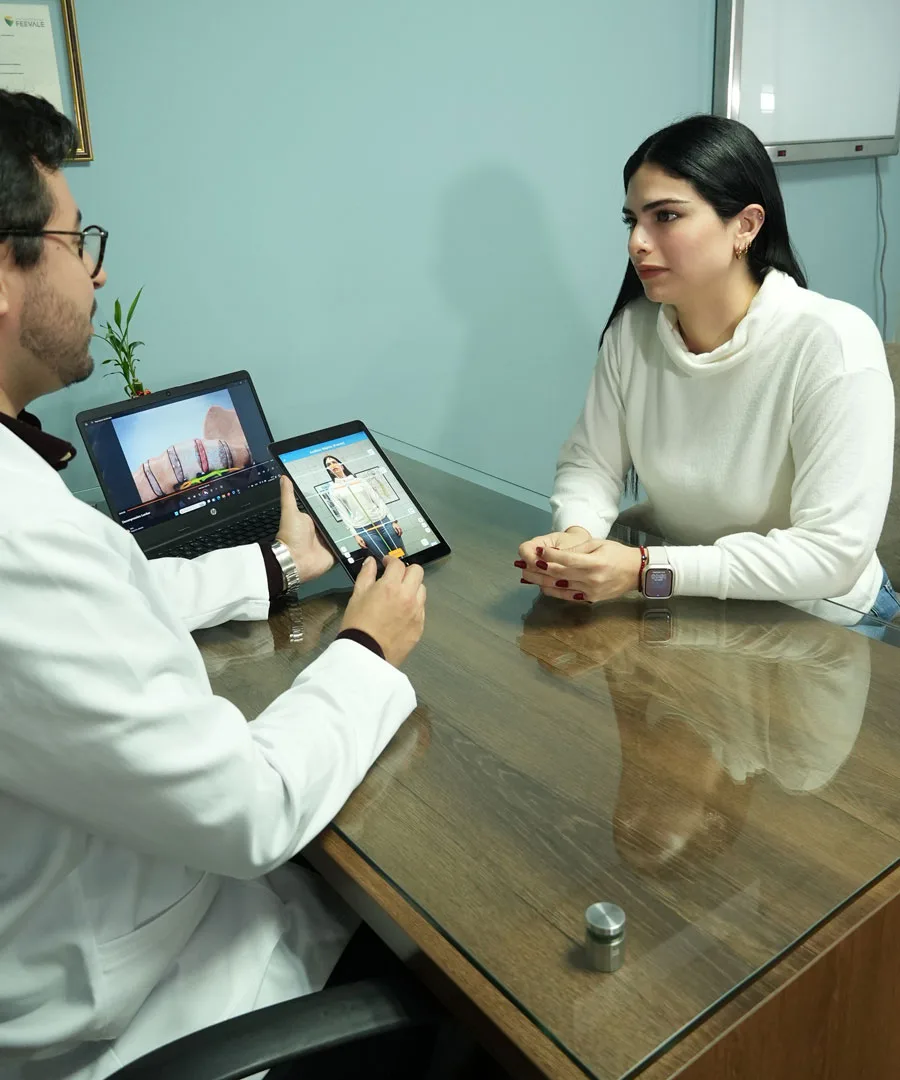 El quiropráctico conversa con una paciente en el consultorio, con una columna en la pantalla del portátil